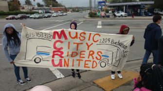 Three teenagers holding up a Music City Riders United banner